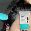A tube of PDRN Reedle Shot Brush Hair Serum for daily scalp care is shown next to a black hair, with a brush visible in the b