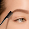 Primer plano de una mano sosteniendo un cepillo para controlar los bordes de cabello negro de doble cara cerca de un ojo.