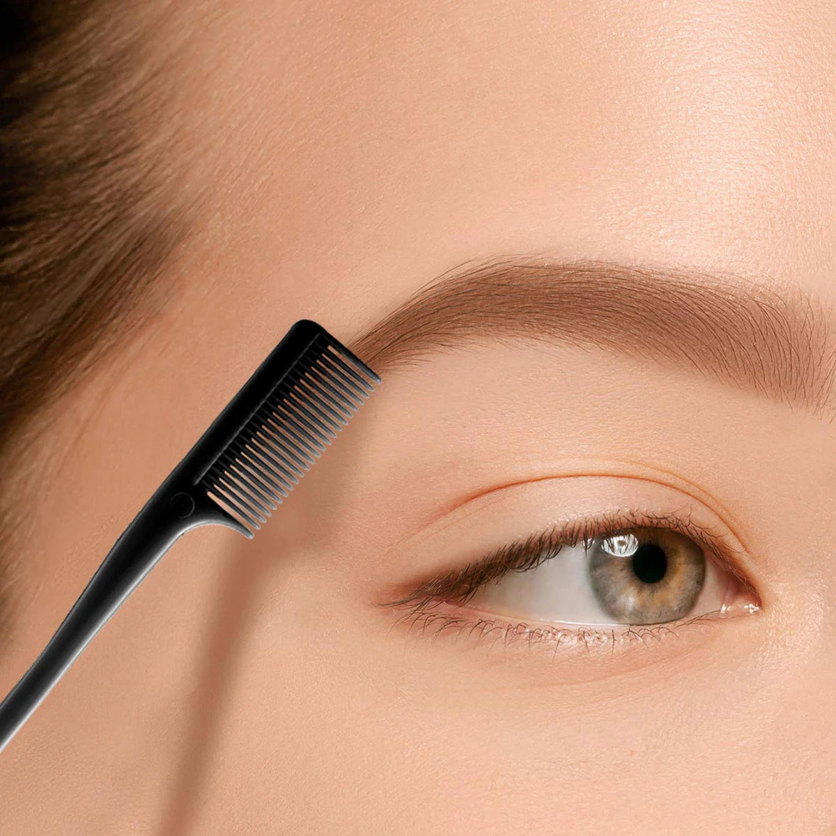Primer plano de una mano sosteniendo un cepillo para controlar los bordes de cabello negro de doble cara cerca de un ojo.