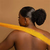 A woman shows off a bright yellow exfoliating mesh body scrub applied across her bare shoulder and back.