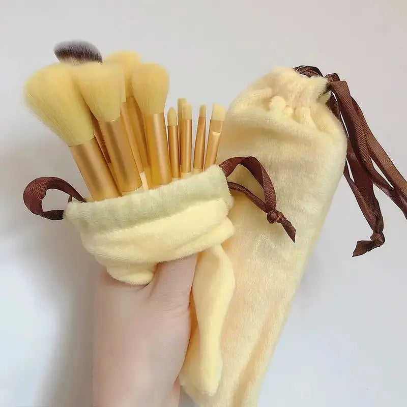 A hand holds a yellow makeup brush set with brown ties and bristles against a white background.