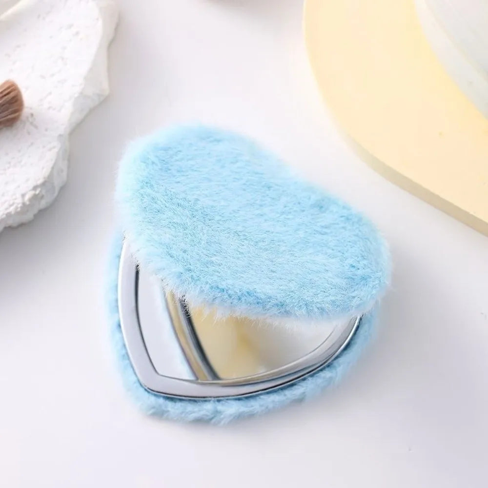 A heart-shaped foldable travel makeup mirror covered in fluffy light blue faux fur.
