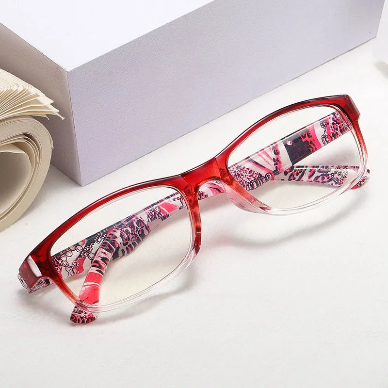 A pair of retro style anti-blue light reading glasses with pink and black floral patterns resting on a white surface.