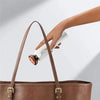 A hand is holding a white red light therapy device inside a brown leather handbag.