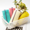 A collection of colorful exfoliating body scrub sponges in pink, blue, and yellow are displayed with greenery.