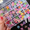 A hand holds an open clear plastic box filled with colorful floral resin nail charms for crafting