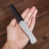 A hand holds a silver foldable anti-static steel comb with black teeth on a wooden surface.