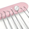 A set of professional multi-tool tooth cleaning instruments with silver tips and a reflective mirror on a pink tray.