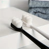 A black toothbrush with white bristles rests on a white surface next to a white toothbrush.