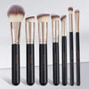 A set of seven professional makeup brushes with gold ferrules and black handles displayed vertically.