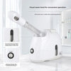 A white facial steamer device with a visual water level window and an on/off switch is shown on a marble surface.