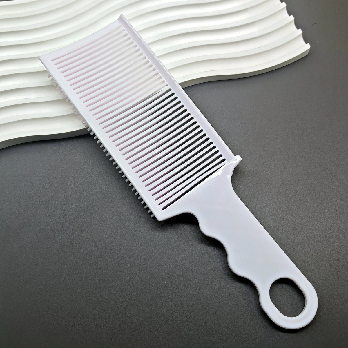 A white professional barber hair cutting comb with a handle is shown next to a white striped headband.