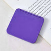 A purple double-sided portable makeup mirror lying on a white surface next to a piece of paper.