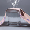 Una taza de vidrio transparente con una banda de tela rosa alrededor, emitiendo una pluma de vapor tenue.