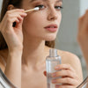 A woman applies a liquid product onto her face using a precision wooden cotton swab.