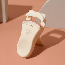 Un recourbe-cils à griffes de chat beige sur une surface rose pâle.