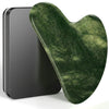 A green jade gua sha tool resting on a dark gray rectangular surface.