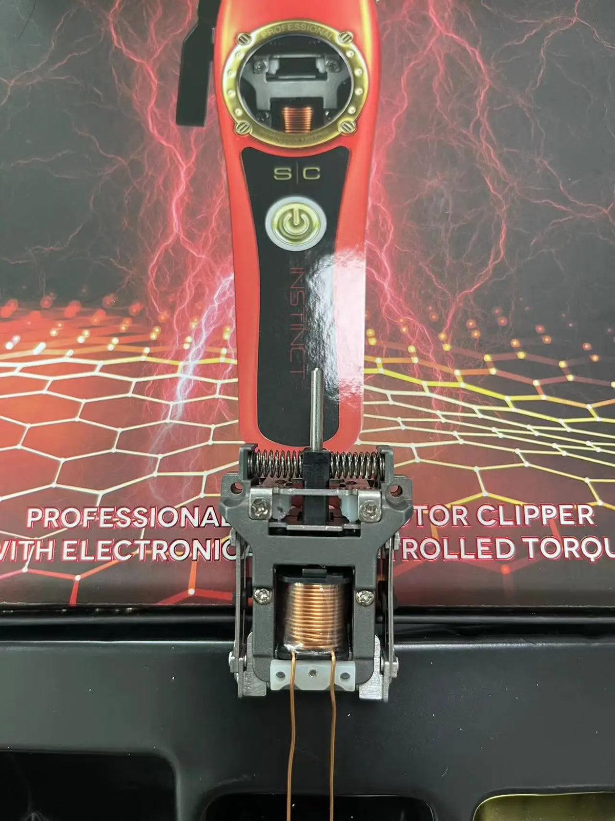 A close-up of a red professional electric hair trimmer with a metallic clipper attachment and wires.