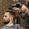 A man is using a professional beard styling brush on another man's beard.