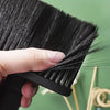 A hand holds a black soft bristle hair duster brush against a light green background.