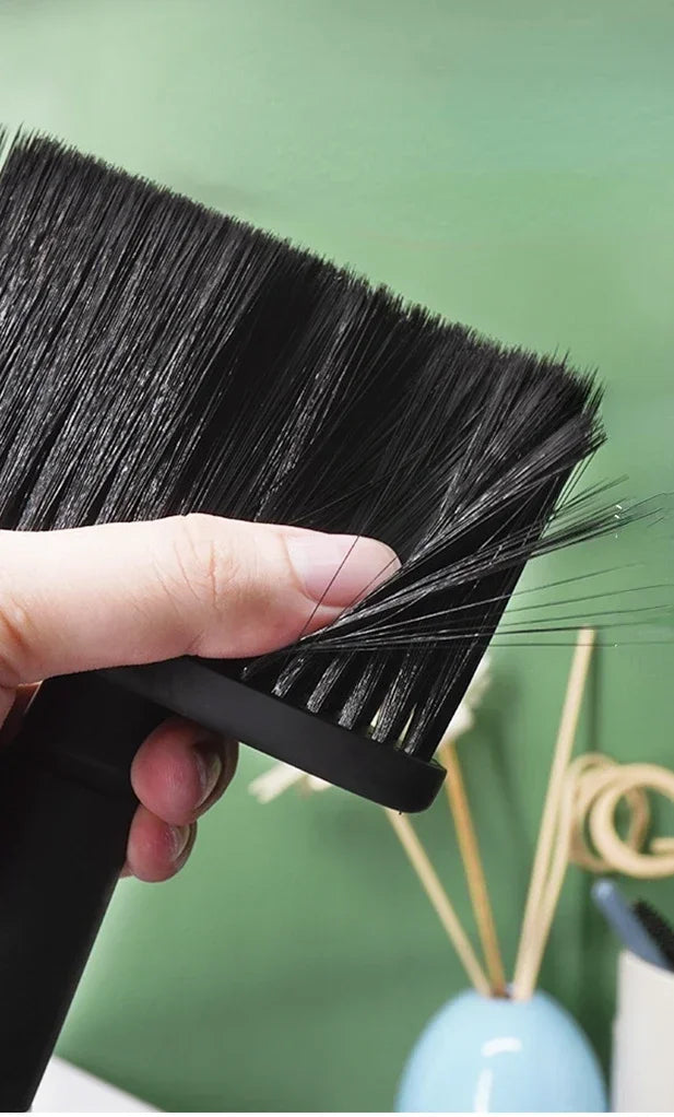 A hand holds a black soft bristle hair duster brush against a light green background.