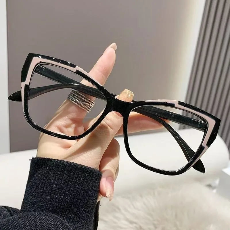 Une main tient une paire de lunettes à monture de chat noir et blanc sur un fond clair.