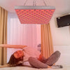 Una persona acostada en la cama bajo un panel de fototerapia LED rojo.