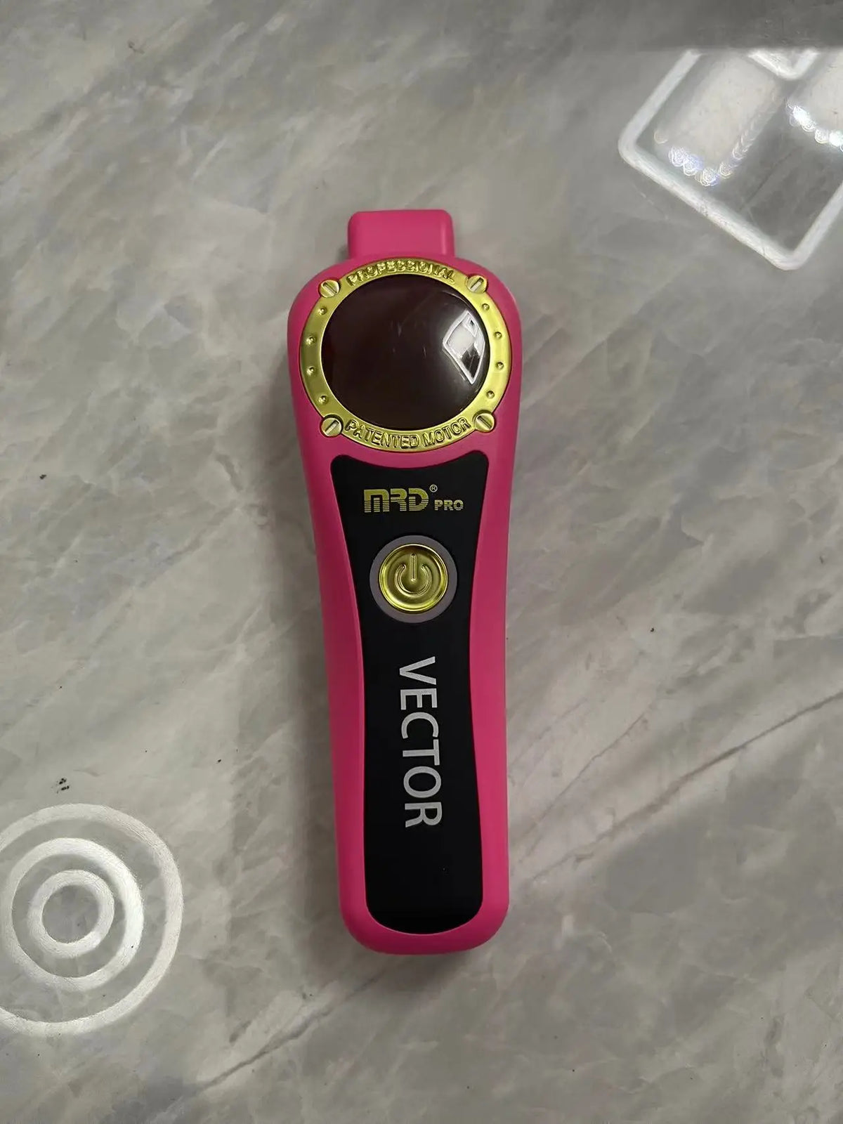 A pink and black professional electric hair trimmer with a gold accent and a power button is shown on a light surface.