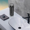 A black portable electric shaver is placed on a white countertop next to a white sink.
