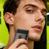 A man holds a compact shaver with precision trimmer against his face, demonstrating its use.