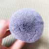 A close-up of a fluffy, purple bamboo airbrush foundation and bronzer brush held in a hand.