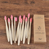 A box containing a set of ten natural bamboo toothbrushes and a pink toothbrush, resting on a wooden surface.