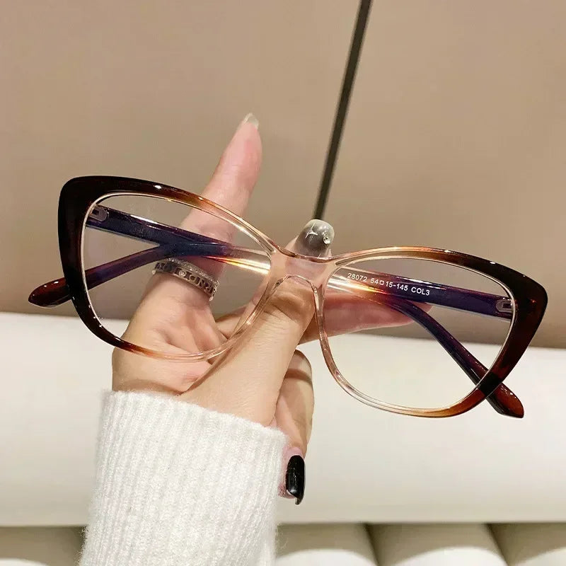 A hand holds a pair of elegant tortoiseshell cat eye reading glasses with purple accents against a light background.