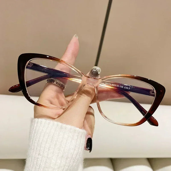 A hand holds a pair of elegant tortoiseshell cat eye reading glasses with purple accents against a light background.