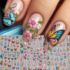 A close-up of a hand displaying long, natural-colored nails decorated with delicate pink and blue flower butterfly nail stick