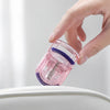 A hand is holding a pink and purple portable mini eyelash curler set above a white surface.