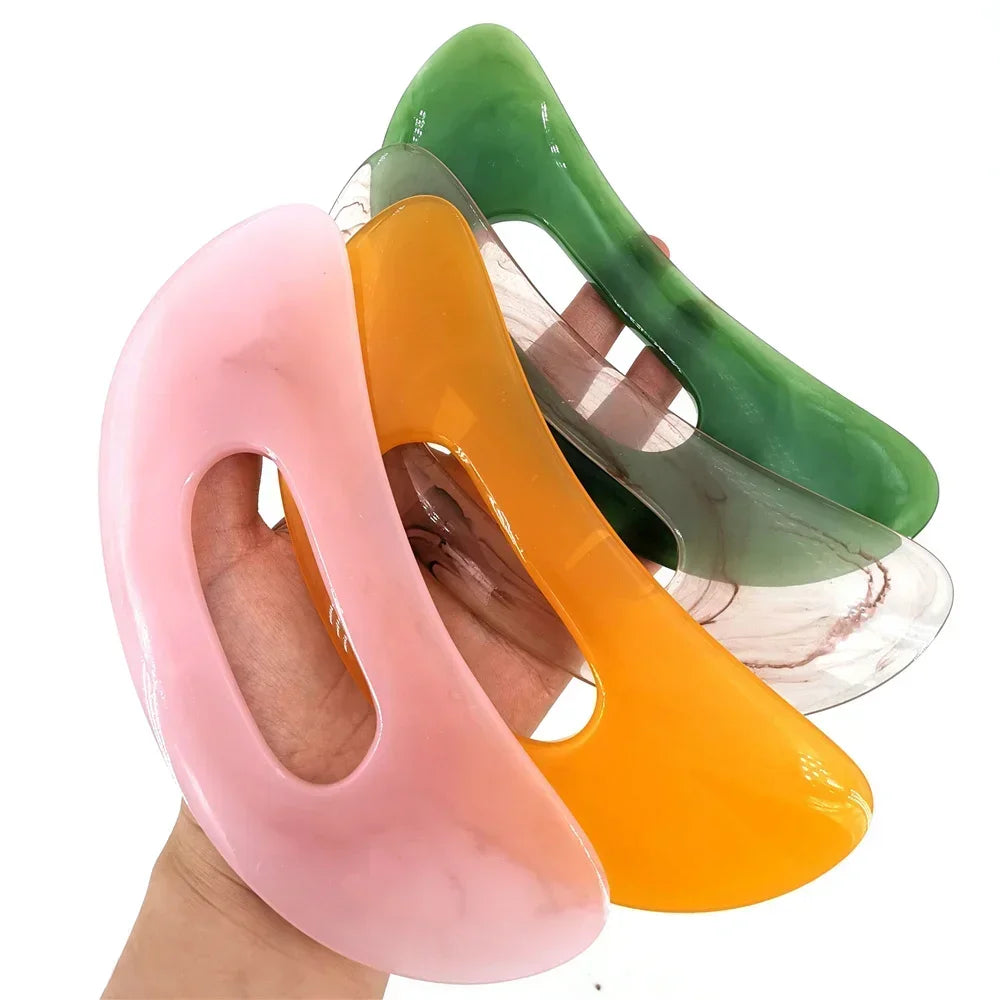 Trois planches de massage Guasha en pierre naturelle rose, orange et vert tenues par une main.