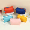 A collection of colorful PU leather makeup bags in orange, blue, yellow, and pink are displayed on a white surface.