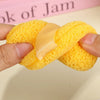 A hand holds a yellow exfoliating cleansing sponge used for blackhead removal.