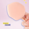 Une main tient un puff de mélange de maquillage rond, couleur pêche, avec une fine ouverture et une pointe en Q épaisse.