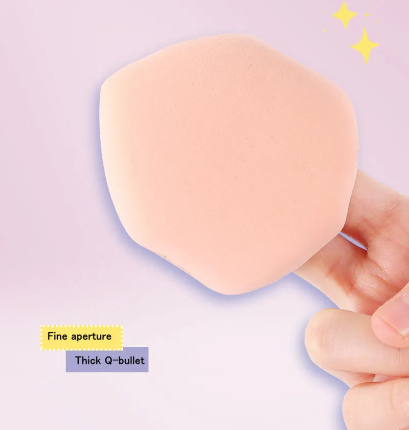 Une main tient un puff de mélange de maquillage rond, couleur pêche, avec une fine ouverture et une pointe en Q épaisse.