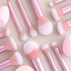 Una colección de 12 brochas de maquillaje profesionales en tonos rosa y blanco, dispuestas sobre un fondo claro.