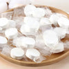 A collection of white reusable compressed face towels packaged in clear plastic resting on a wooden board.