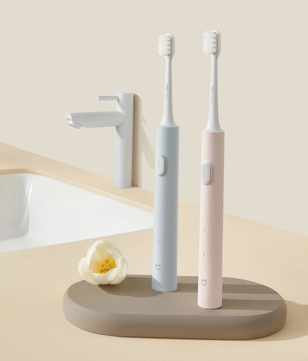 A pair of pink and light blue sonic electric toothbrushes are displayed next to a white sink and faucet.