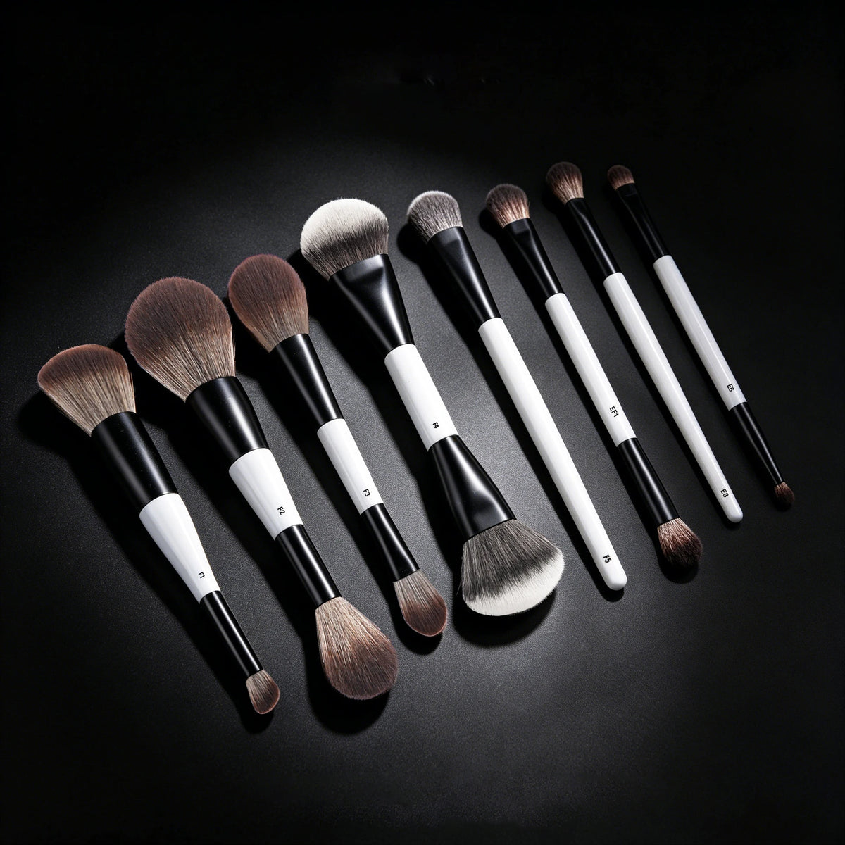 A collection of black and white dual-ended makeup brushes for foundation and contour displayed on a dark surface.