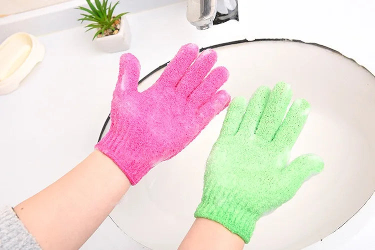 Une main portant un gant exfoliant rose vif à côté d'un gant exfoliant vert lime sur une surface blanche.