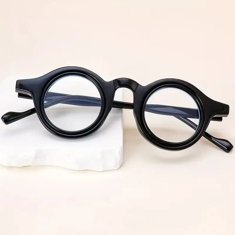 Une paire de lunettes de lecture transparentes à monture noire ajustables posées sur une surface blanche.