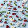 A collection of embossed floral nail art stickers featuring spring designs like bees, flowers, and leaves on a light blue bac