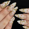Press-on-Falschnägel mit zarten rosa und weißen Mandelblumen und goldenen Akzenten auf einer Hand.