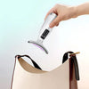 A hand holds a portable facial and neck massager with multi-color lights above a beige cosmetic bag.